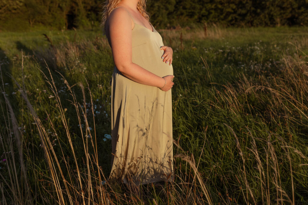 Close-up van een zwangere vrouw in een groene jurk die haar buik vast houdt.