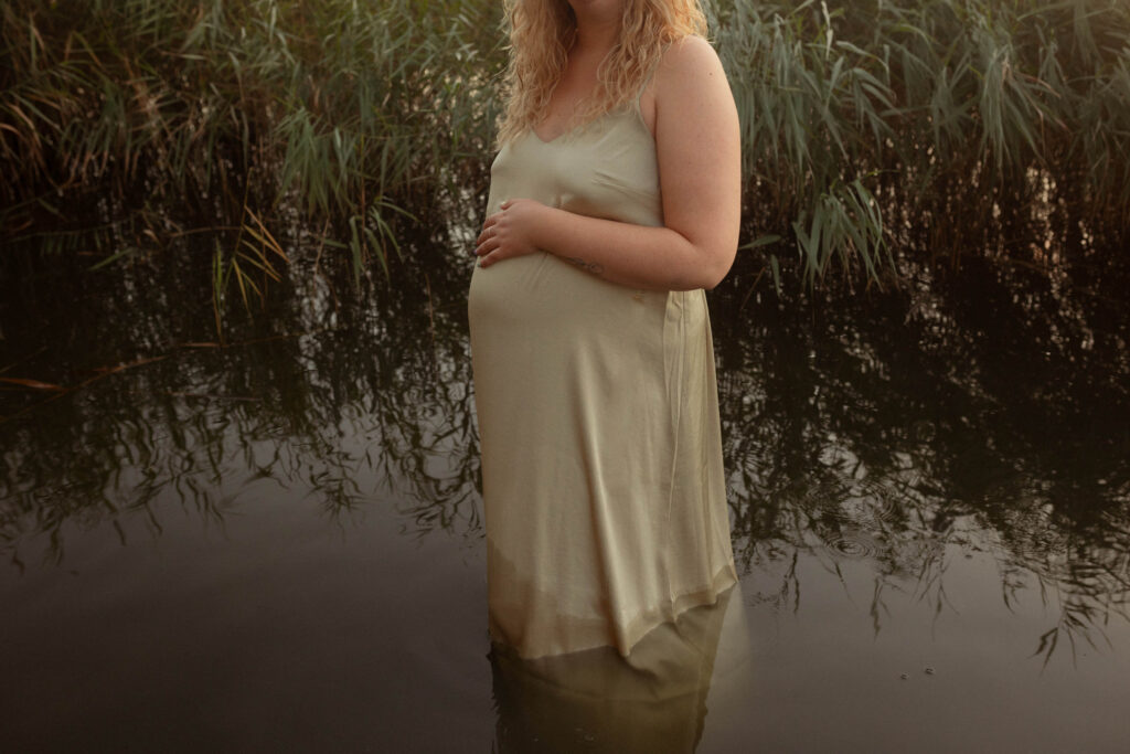 Zwangere vrouw staat in water met hand liefdevol op haar buik