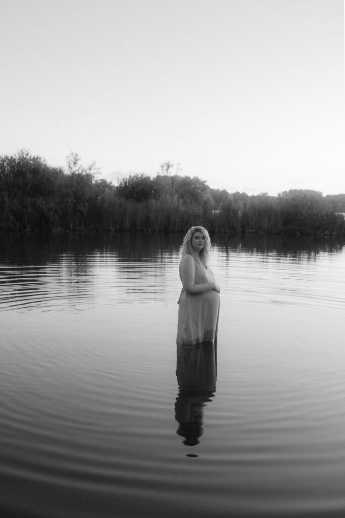 Een zwnagere vrouw staat tot haar knieën in het water.