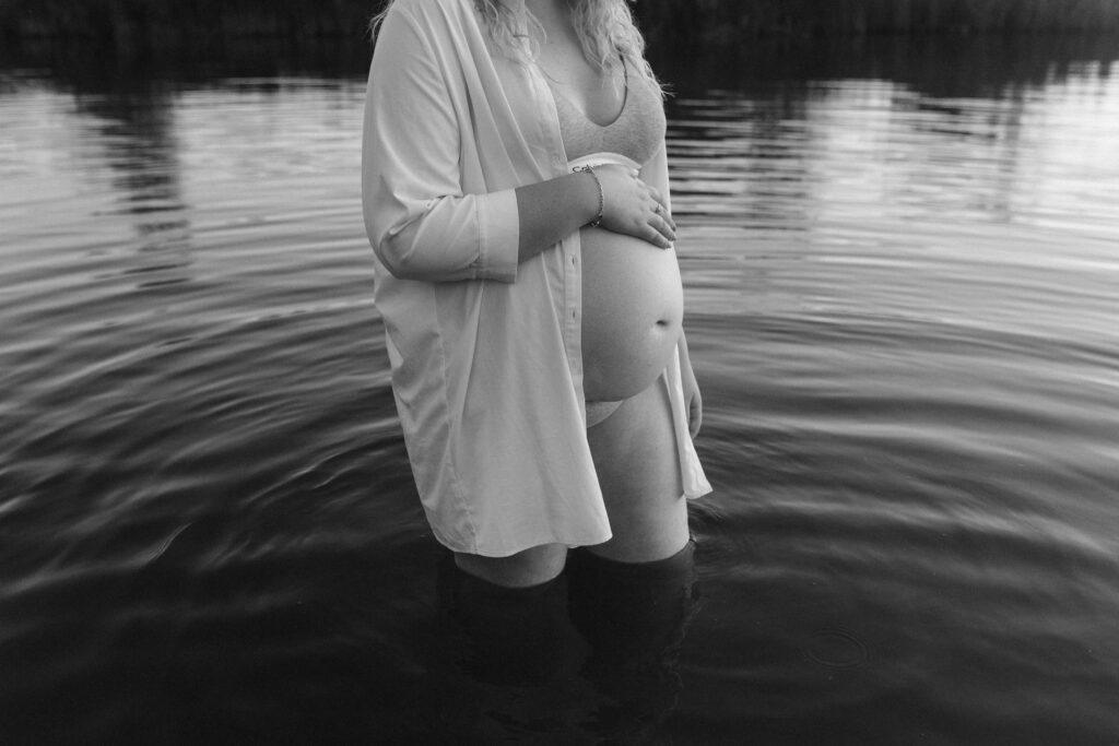 Zwartwit beeld van een zwangere vrouw met een witte blouse die poseert in het water